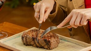Manos de una persona cortando un filete de carne sobre una tabla de madera.