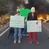 Cuatro personas sostienen carteles de protesta en una carretera bloqueada por fuego y humo; los mensajes exigen justicia y la aparición de personas.