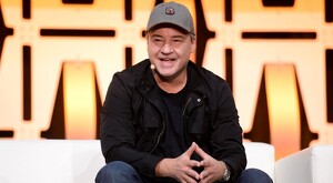 Vince Zampella viendo de frente mientras sonríe delante de letrero luminoso amarillo durante una presentación pública