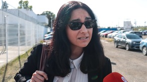 Una mujer con gafas oscuras hablando frente a un micrófono rojo en una tarde soleada.