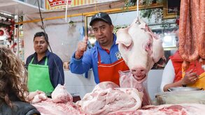 Un hombre en una carnicería mostrando la cabeza de un cerdo.