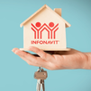 Una mano sostiene una pequeña casa de madera con el logotipo de INFONAVIT impreso en rojo, junto a un juego de llaves, sobre un fondo azul claro.