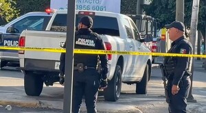 Dos oficiales de la Policía Municipal de Guadalajara detrás de una cinta policiaca amarilla, una camioneta blanca y una patrulla policial