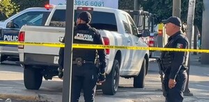 Dos oficiales de la Policía Municipal de Guadalajara detrás de una cinta policiaca amarilla, una camioneta blanca y una patrulla policial