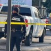 Dos oficiales de la Policía Municipal de Guadalajara detrás de una cinta policiaca amarilla, una camioneta blanca y una patrulla policial