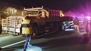 Personas caminbando sobre una carretera de noche, junto a un camión de volteo.