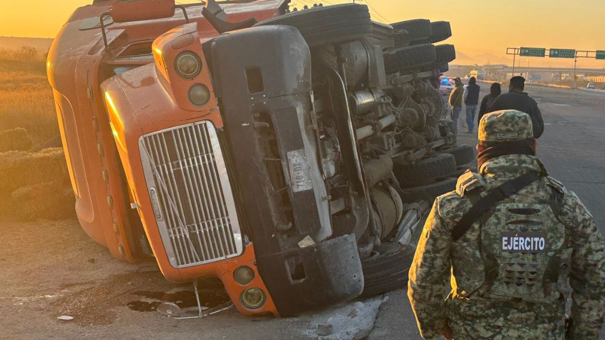 Tráiler color naranja volteado, transportaba alfafa, en el amanecer.