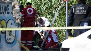 Grupo de paramédicos reunidos alrededor de una persona sin vida en un camino de terracería.