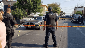 Agentes de policía custodian una escena del crimen acordonada con cinta amarilla; se observan marcadores de evidencia numerados sobre el pavimento.