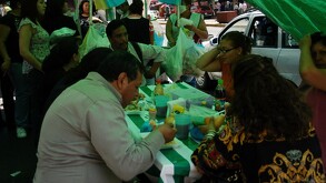 Se observa a varias personas, entre hombres y mujeres, sentados en una mesa comiendo.