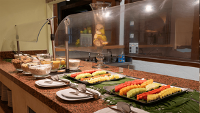 Barra de autoservicio con cortes de sandía, melón y piña, acompañada de una variedad de granolas y semillas.