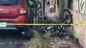 Motocicleta negra volcada sobre la banqueta al lado de un automóvil rojo de la marca Renault y detrás de una cinta policiaca