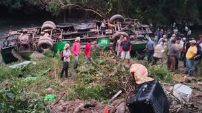Personas alrededor de un autobús de pasajeros volcado en un río de Veracruz.