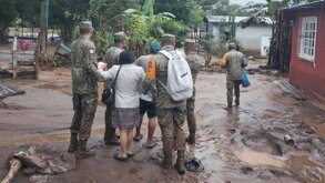 Militares resguardan a una mujer en un camino inundado por la lluvia.