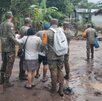 Militares resguardan a una mujer en un camino inundado por la lluvia.