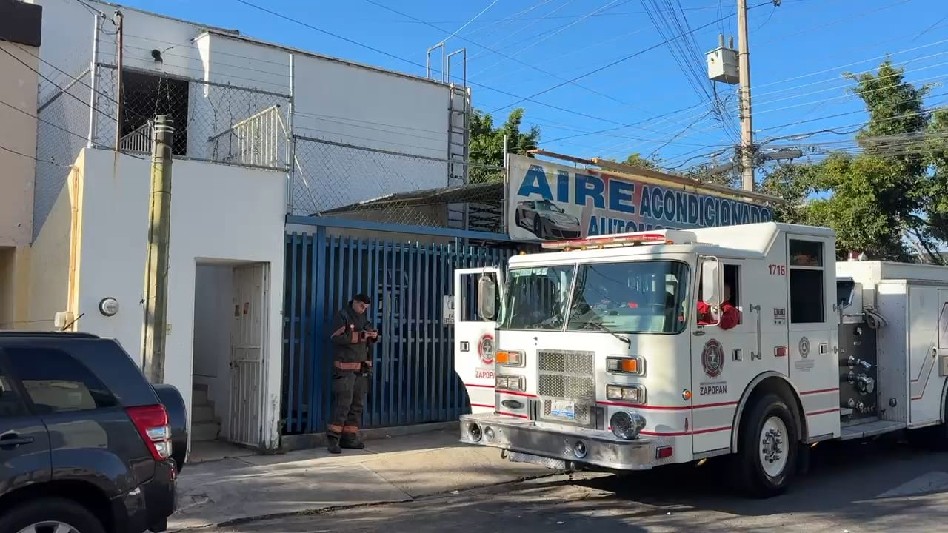 Bombero y camión blanco de Protección Civil de Zapopan enfrente de una reja azul y un letrero de aire acondicionado