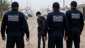 Tres policías municipales de Tlajomulco vistos de espaldas deteniendo a un adolescente con patrullas de policía en el fondo