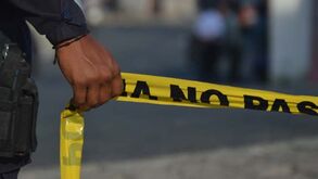 Policía sostiene con su mano la cinta para acordonar la escena del crimen.