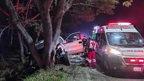 Una ambulancia de la Cruz Roja con luces encendidas atiende un fuerte choque nocturno donde una camioneta blanca se impactó contra un árbol.