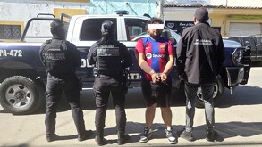 Joven con playera del Barcelona con los ojos censurados y esposas en las manos con policías de Jalisco a los lados