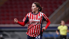 Una jugadora del equipo femenil de las Chivas del Guadalajara corre por la cancha vistiendo el icónico uniforme de rayas rojas y blancas.