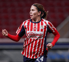 Una jugadora del equipo femenil de las Chivas del Guadalajara corre por la cancha vistiendo el icónico uniforme de rayas rojas y blancas.