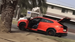 Un vehículo deportivo de lujo color naranja brillante se encuentra estacionado junto a una palmera con la puerta y la cajuela abiertas.