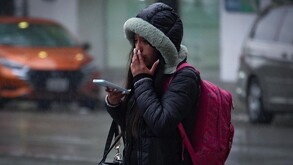 Se observa a una joven con una chamarra de gorro color negro con gris.