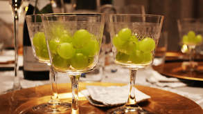 Tres copas de cristal llenas de uvas verdes se encuentran dispuestas sobre platos dorados en una mesa decorada para una celebración de Año Nuevo.