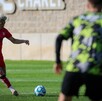 Un jugador de fútbol del equipo Atlas con uniforme rojo entrena en una cancha de pasto, preparándose para patear el balón durante el día.