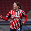 Una jugadora del equipo femenil de las Chivas del Guadalajara corre por la cancha vistiendo el icónico uniforme de rayas rojas y blancas.