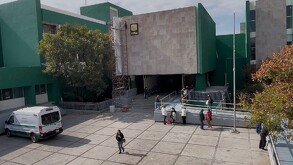Se observa un edificio color beige con verde y unas personas caminando.