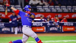 Un bateador de los Charros de Jalisco, con casco azul y guantes rojos, completa un potente swing durante un partido nocturno de béisbol.
