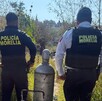 Dos agentes de la Policía de Morelia aparecen de espaldas en un terreno baldío junto a un tanque de gas metálico que se encuentra en el suelo.