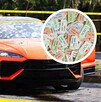 Un auto deportivo naranja con impactos de bala en el parabrisas está acordonado; un círculo superpuesto muestra boletos de rifa de colores.