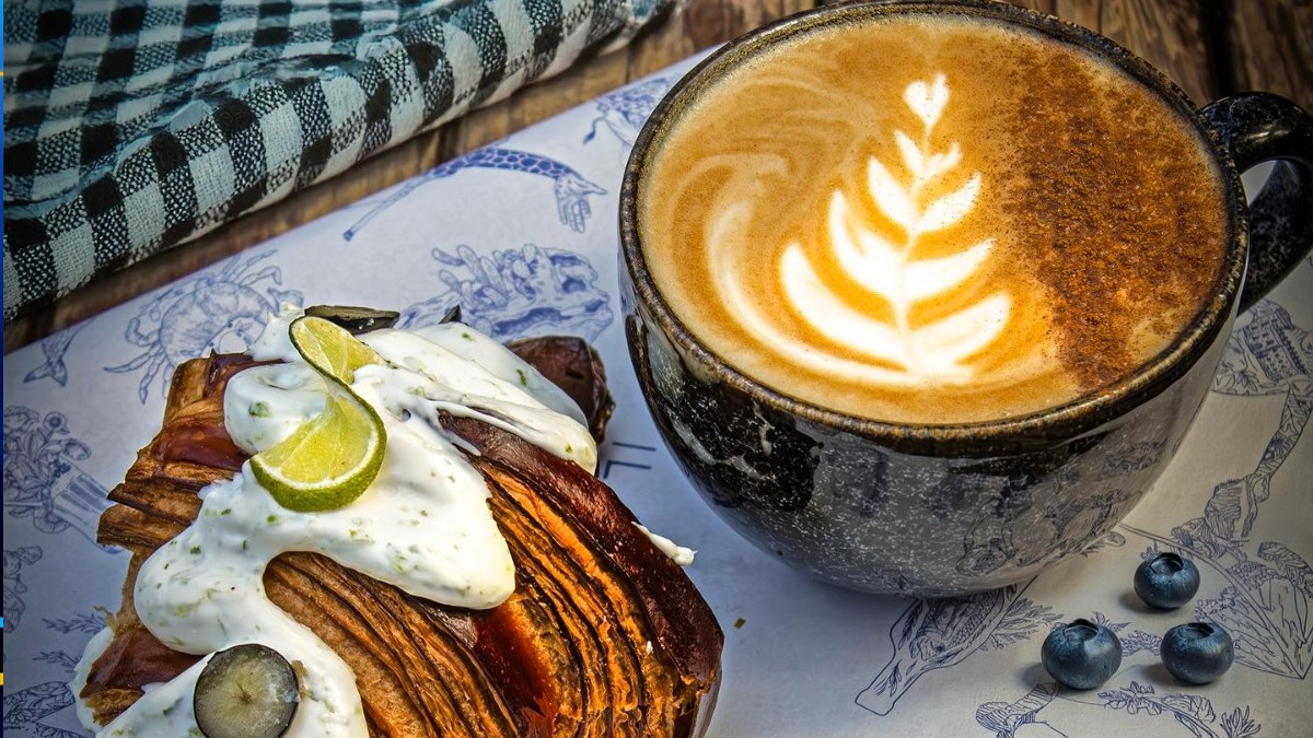 Se observa una taza con café y un pan como croissant a lado.