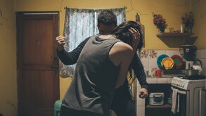 Se ve a un hombre y una mujer, no se les distingue el rostro, dentro de una casa.