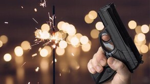 Una mano sostiene una pistola negra en primer plano, mientras al fondo una bengala chispeante brilla contra un efecto de luces desenfocadas.