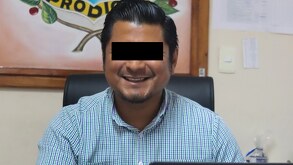 Un hombre con los ojos cubiertos, junto a computadora portátil y un reloj de arena.