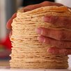 Una mano humana acomoda una serie de tortillas en una báscula.