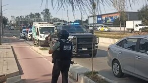 Un agente de la Guardia Nacional vigila una vialidad donde se observa un convoy de patrullas y una ambulancia con las luces de emergencia encendidas.