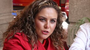 Mujer de cabello rizado con una prenda roja y gesticulando una expresión mientras habla.