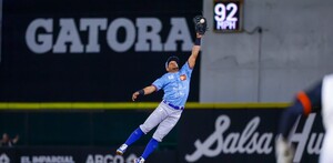 Un jugador de los Charros de Jalisco salta espectacularmente con el guante extendido para atrapar una pelota durante un juego nocturno.