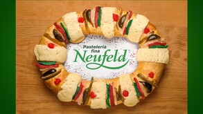 Una tradicional Rosca de Reyes con fruta cristalizada y costras de azúcar sobre una mesa, con el logotipo de la 