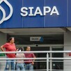 Fachada de una oficina del SIAPA con su logotipo azul y blanco; varias personas esperan afuera detrás de un barandal metálico cerca de la entrada.
