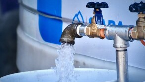 Llave de agua abierta delante de una cisterna del Siapa en Guadalajara con cubetas blancas debajo