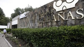 Barda con el nombre del Hogar Cabañas al exterior del edificio con una jardinera y una persona caminando