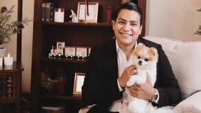 Se observa a un hombre sentado con traje negro y un perro en sus brazos.