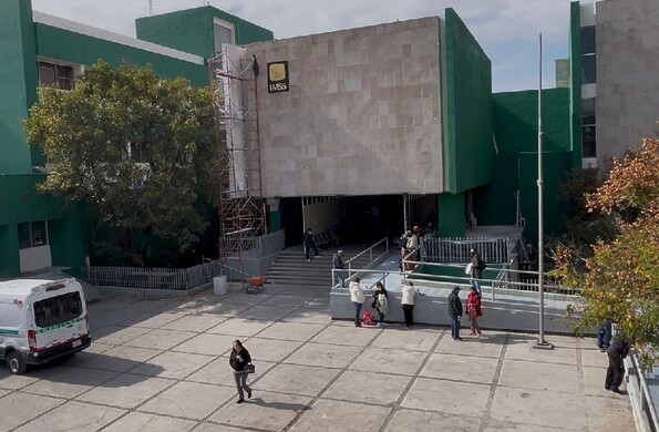 Se observa un edificio color beige con verde y unas personas caminando.