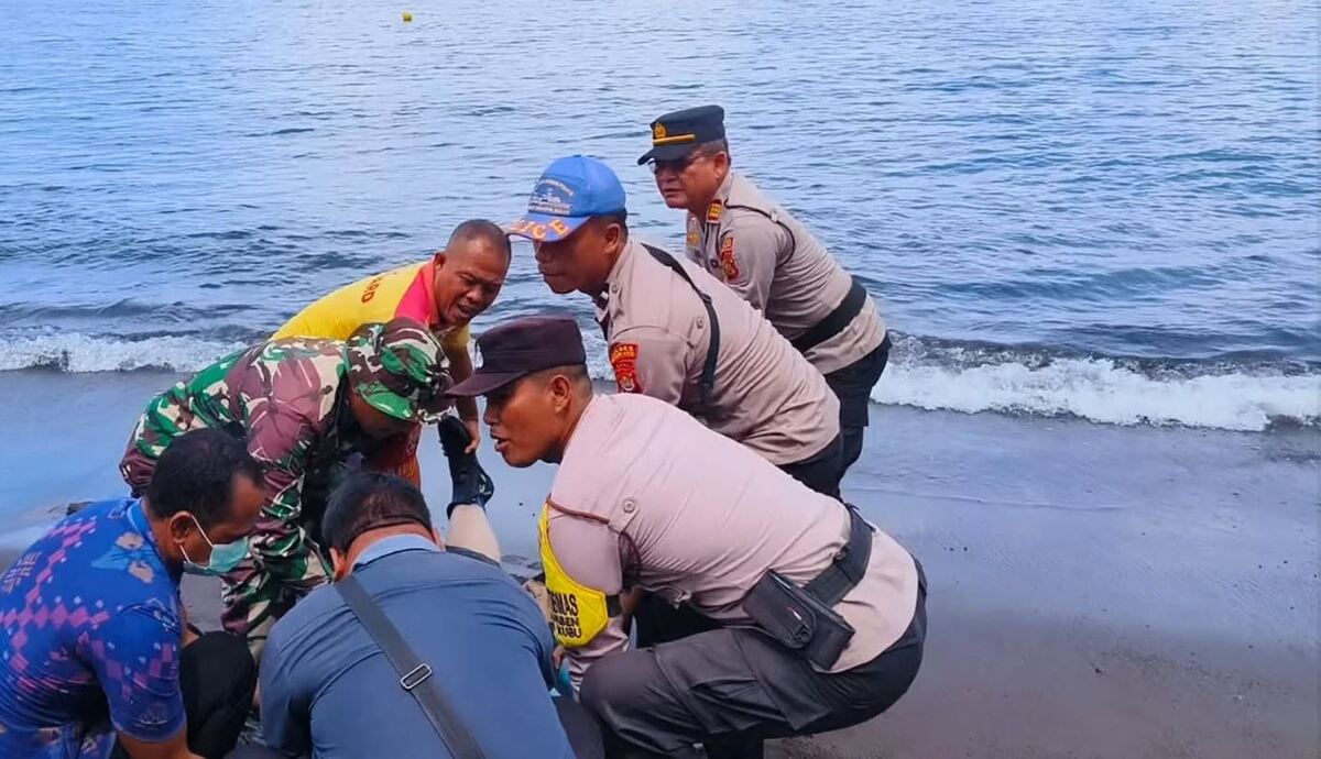Brigadistas de Kubu a la orilla del mar en una playa arrastrando el cuerpo de un hombre fuera del agua